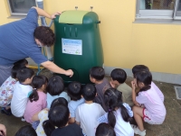 先生から雨水タンクの使用方法を聞く園児たち